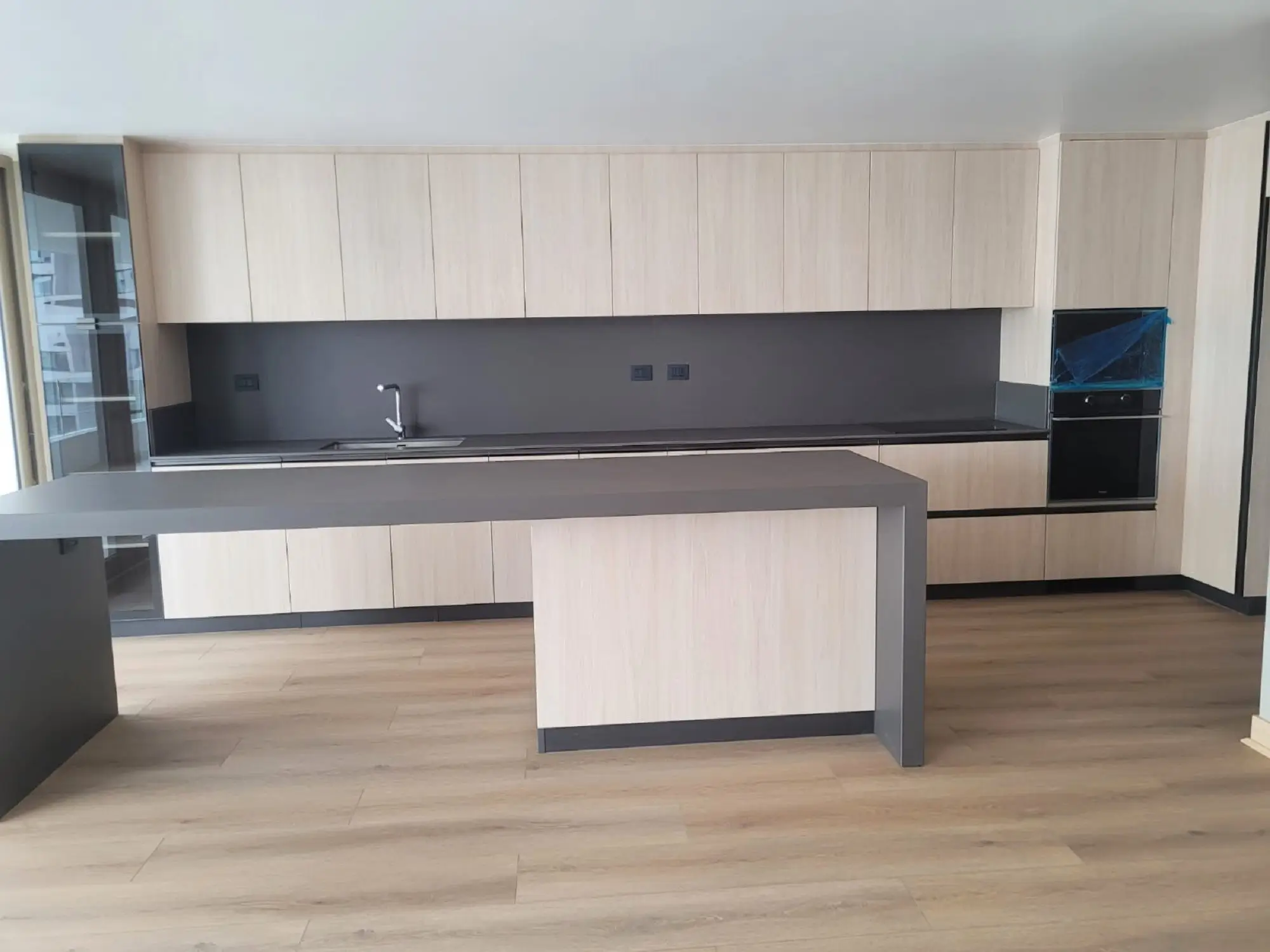 Cocina moderna fabricada en melamina en Chile con gabinetes de madera clara, cubierta de cuarzo gris oscuro y barra tipo isla con iluminación natural